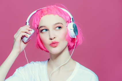 Trendy girl with pink hair enjoys the music on headphones. Pink background. Youth style, leisure.